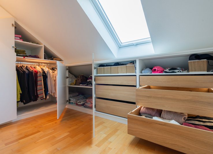Design und Komfort hinter der Front: Den Bereich direkt unter der Dachschräge gestaltete Hennemann mit Fachböden und eleganten Holzschubkästen in Eiche, die auf der Actro 5D-Führung von Hettich laufen (Bild: Markus Gänswein).