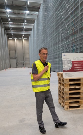 Logistikleiter Matthias Wehle erläutert die Funktionsweise des automatisierten Shuttlelagers, das rechts zu sehen ist (Bild: Kuhn).